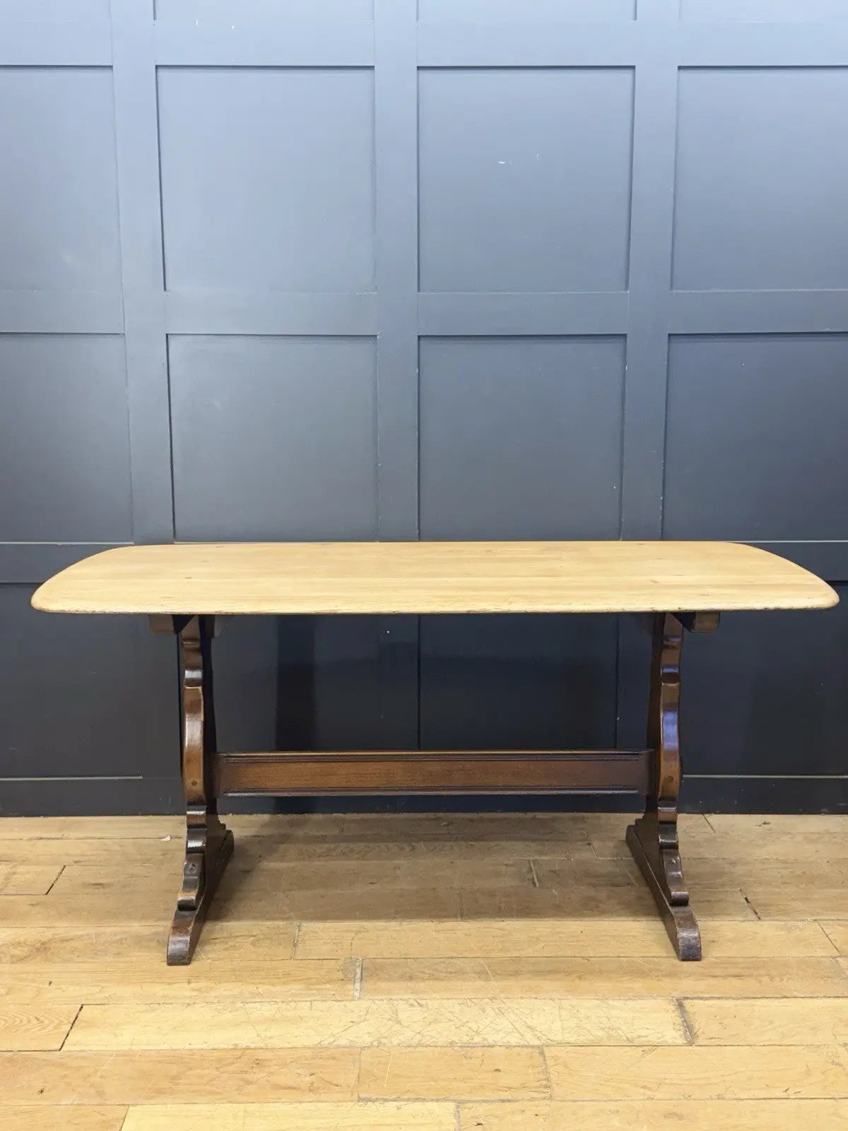 Ercol brown oak refectory dining table with natural wood grain and traditional trestle base.
