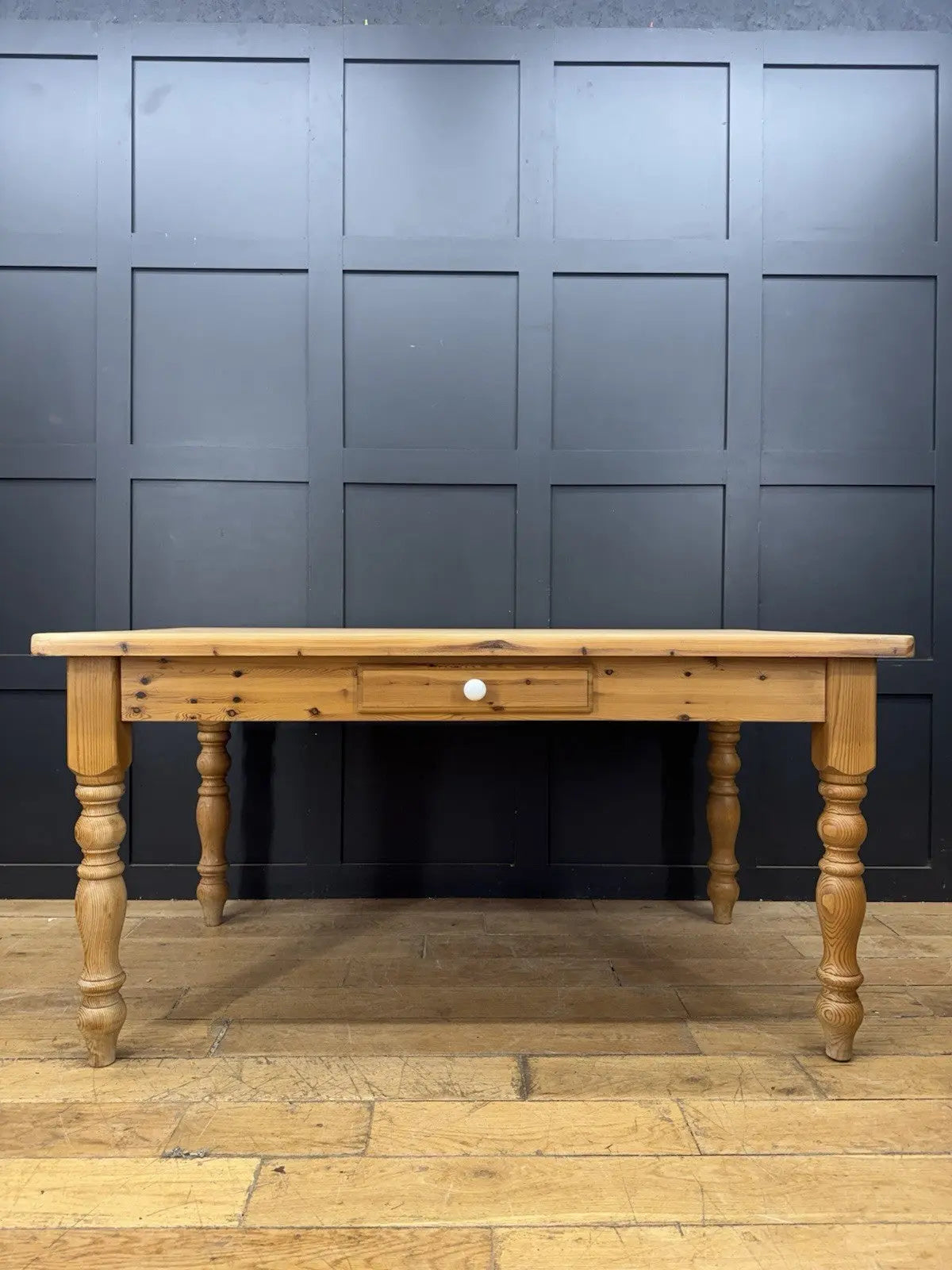 Vintage brown farmhouse dining table with turned legs and central drawer featuring white ceramic knob.