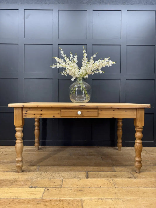Vintage brown farmhouse dining table with turned legs and central drawer featuring white ceramic knob.