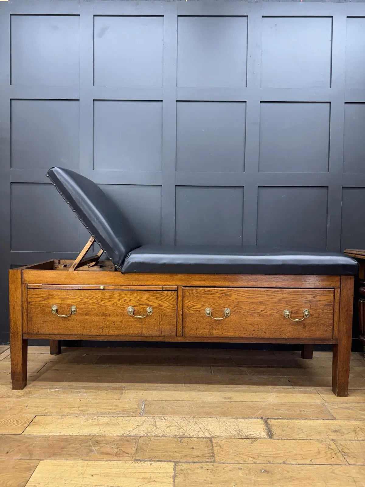 Harris black chaise longue with oak frame, padded Rexine seat, and original maker's plaque.