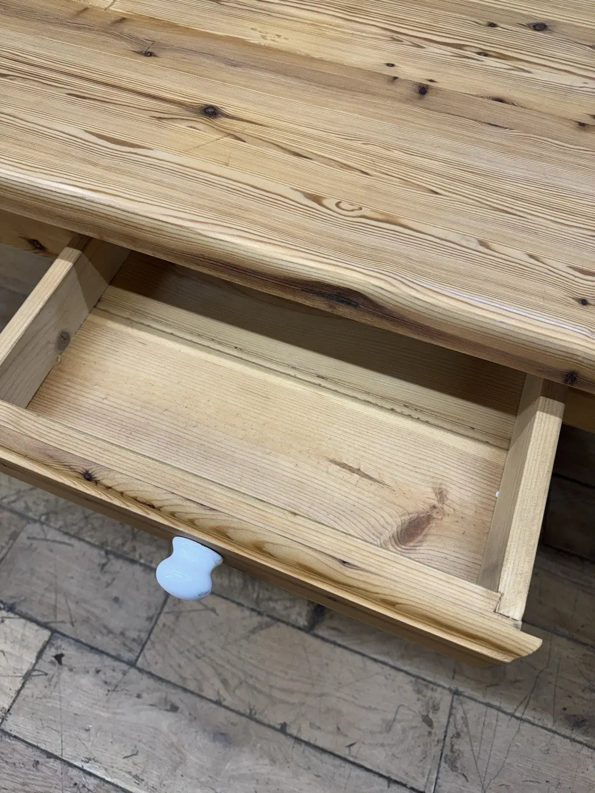 Vintage brown farmhouse dining table with turned legs and central drawer featuring white ceramic knob.