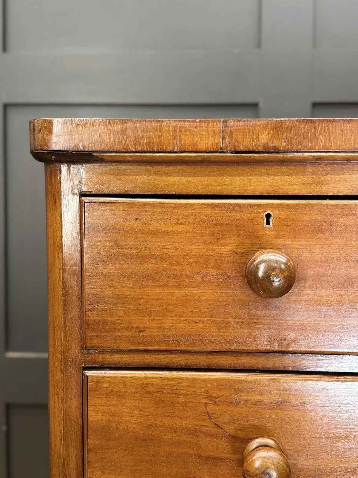 Antique brown mahogany chest of drawers with rounded corners and wooden knob handles.