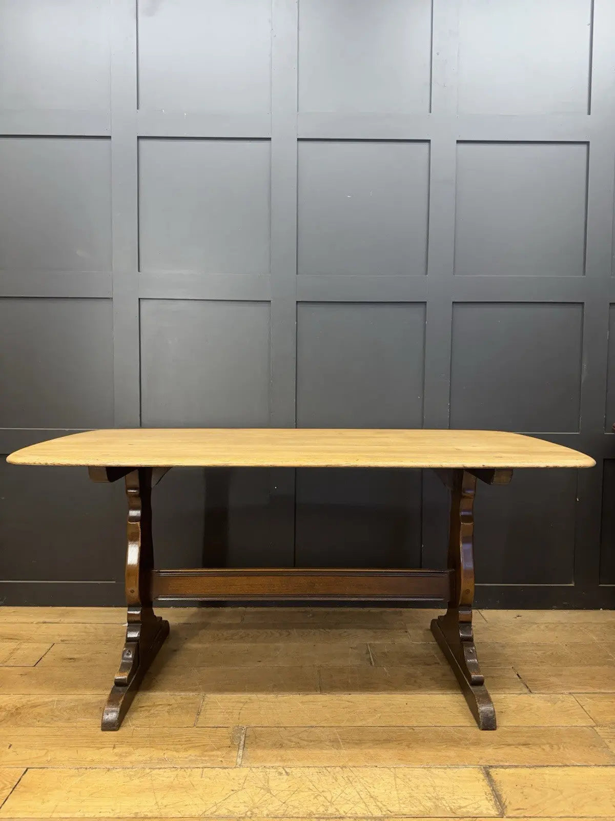 Ercol brown oak refectory dining table with natural wood grain and traditional trestle base.