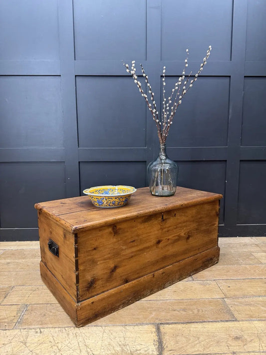 Antique pine hope chest with honey-coloured finish, iron handles, and dovetailed joints.