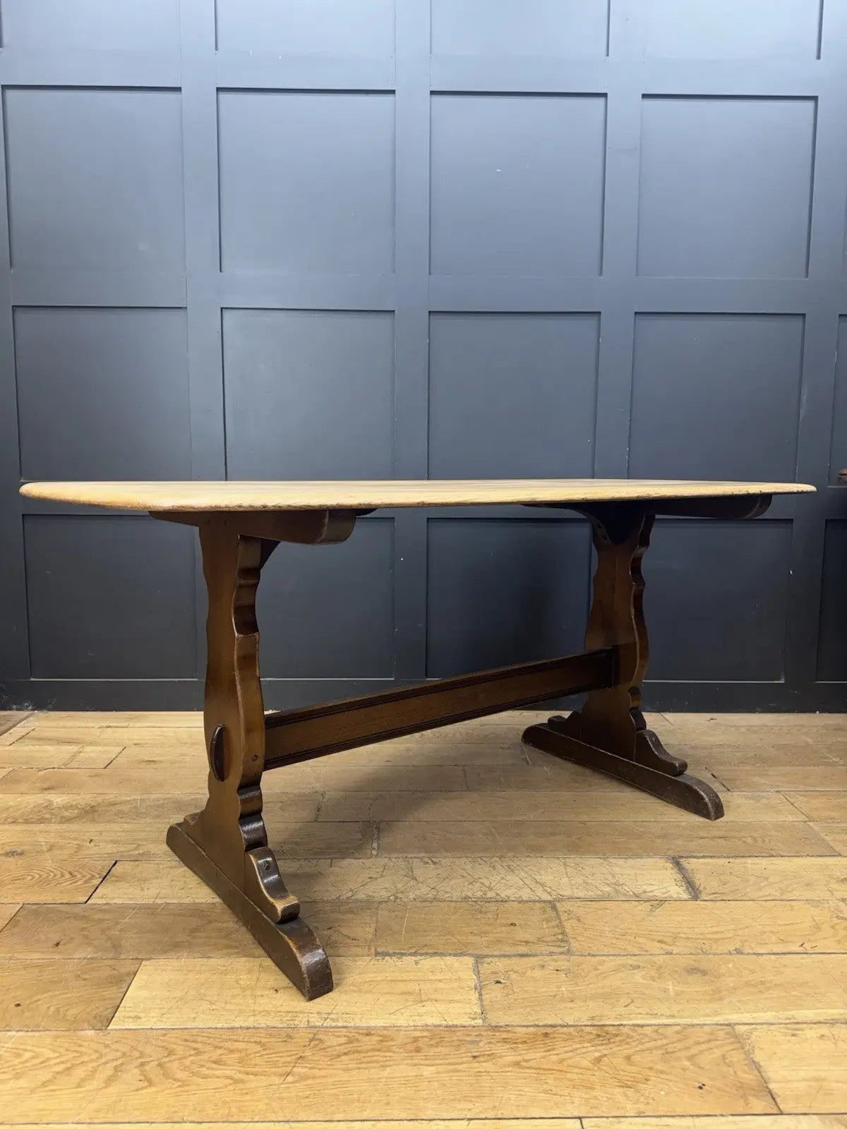 Ercol brown oak refectory dining table with natural wood grain and traditional trestle base.