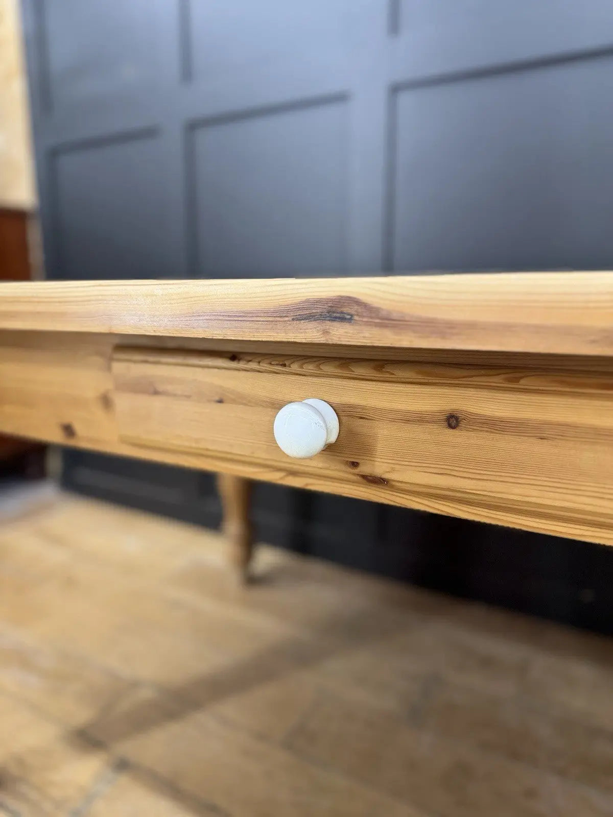 Vintage brown farmhouse dining table with turned legs and central drawer featuring white ceramic knob.