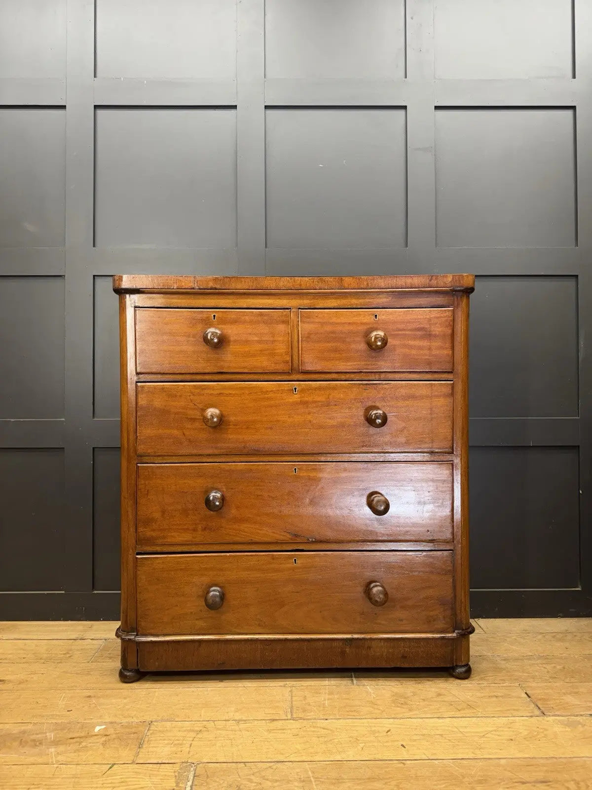 Antique brown mahogany chest of drawers with rounded corners and wooden knob handles.