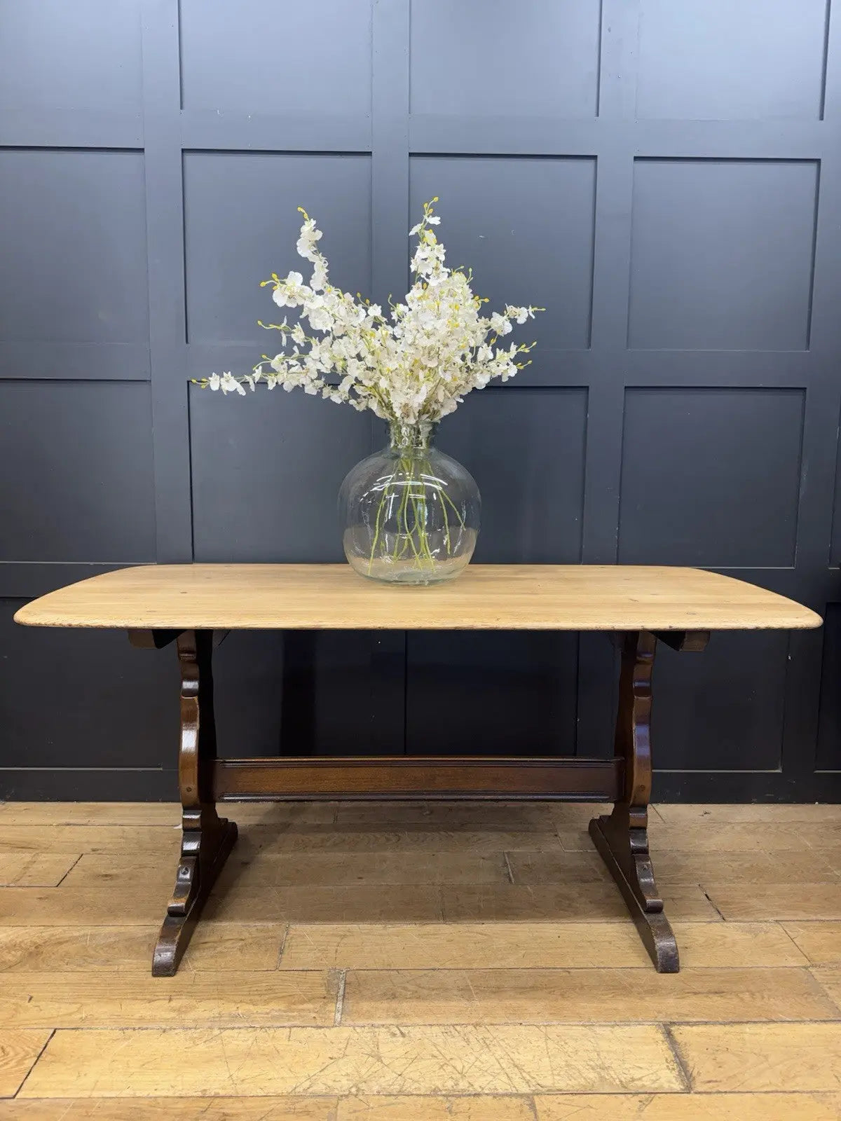 Ercol brown oak refectory dining table with natural wood grain and traditional trestle base.