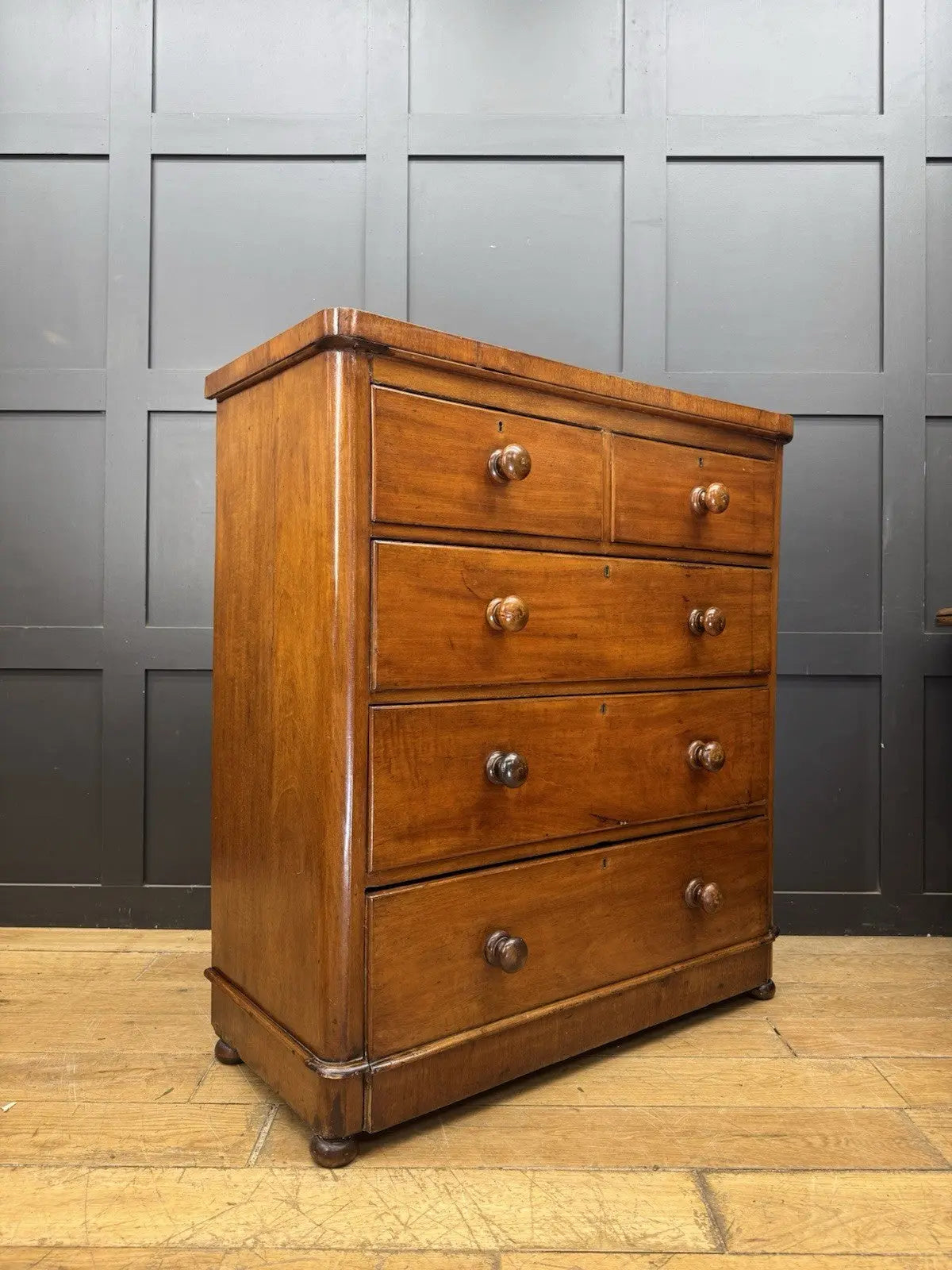 Antique brown mahogany chest of drawers with rounded corners and wooden knob handles.